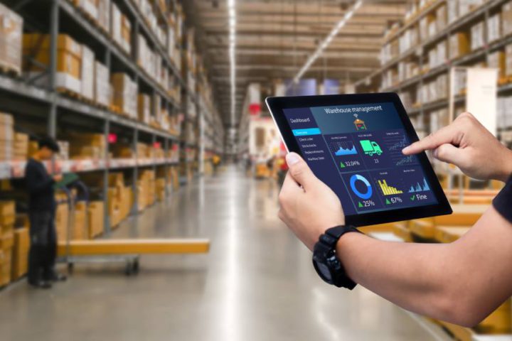 Person holding and touching a tablet showing performance graphics inside a big well organized warehouse full of boxes