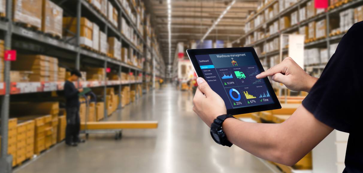 Person holding and touching a tablet showing performance graphics inside a big well organized warehouse full of boxes
